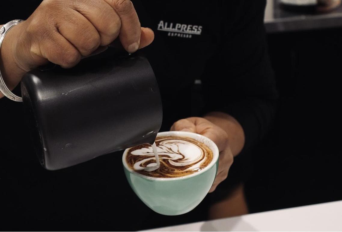 A barista pouring delicate latte art into a mint-green cup